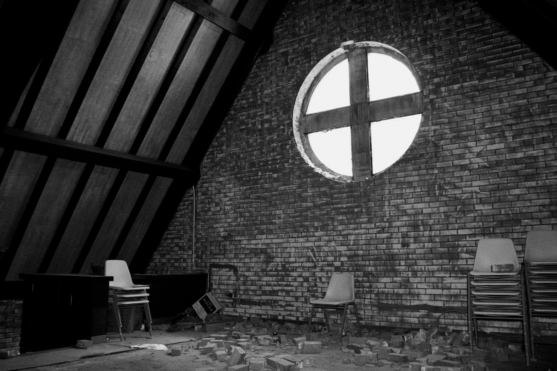 Empty attic room with a round cross-shaped window in a brick wall