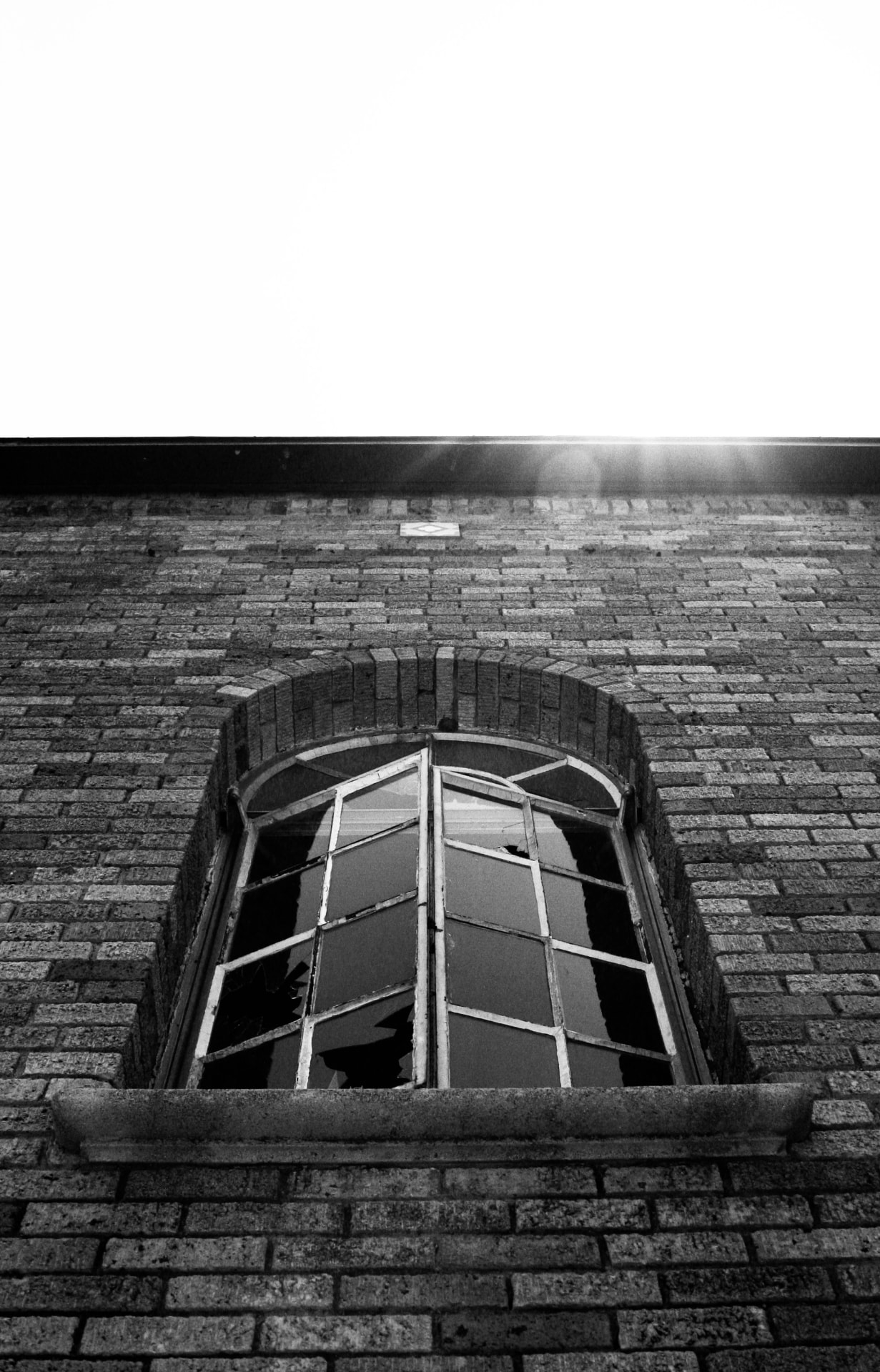 Arched window with broken panes in a brick wall