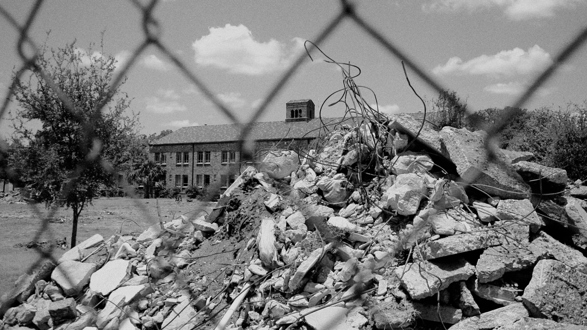 Rubble piled behind a chain-link fence in front of a campus building